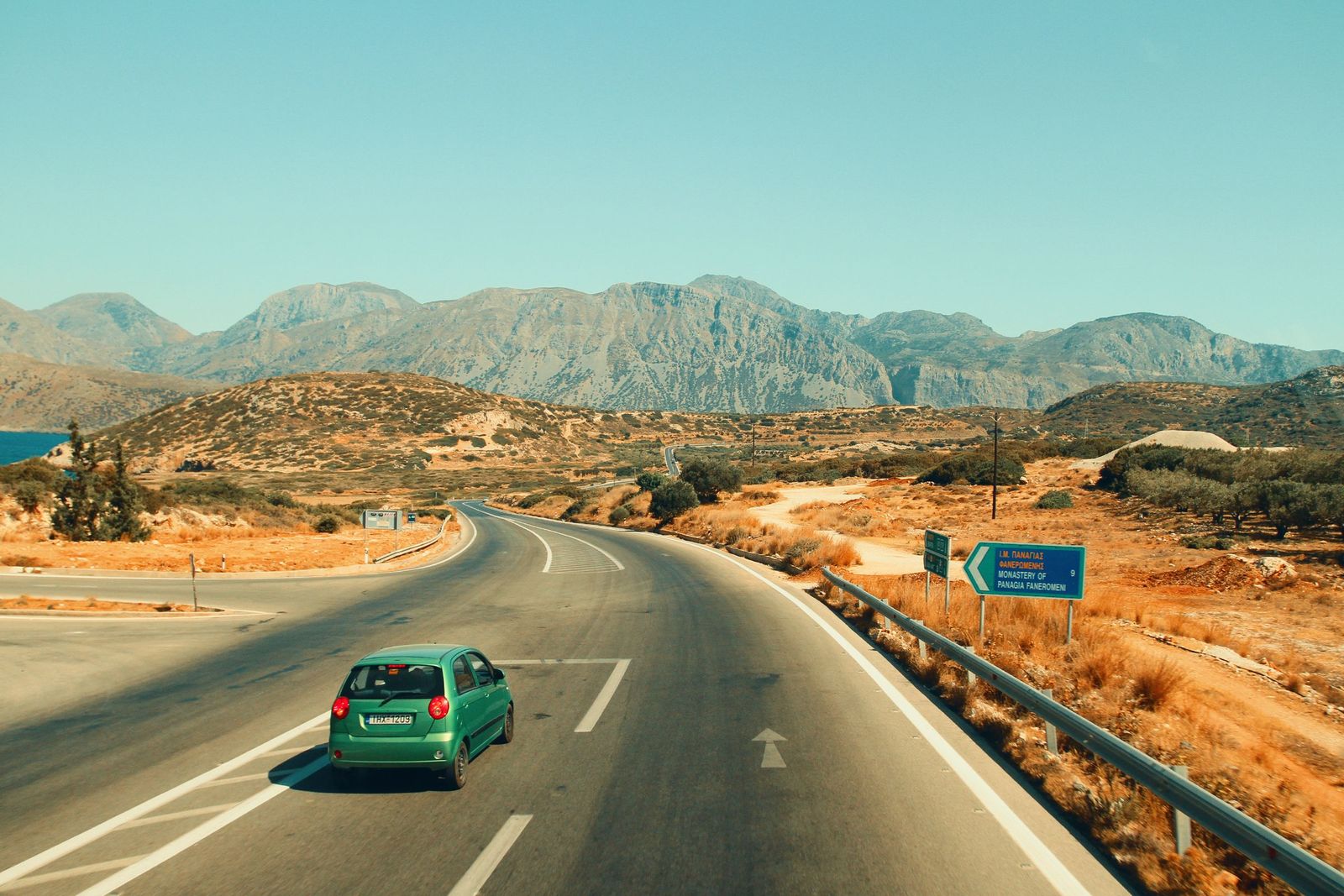 A small green car on a winding road through the mountains