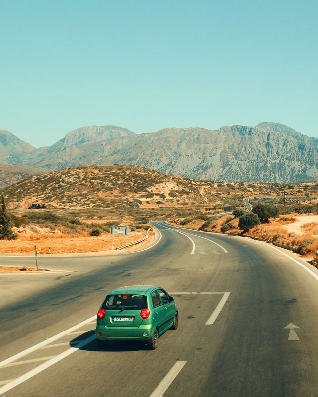 A small green car on a winding road through the mountains