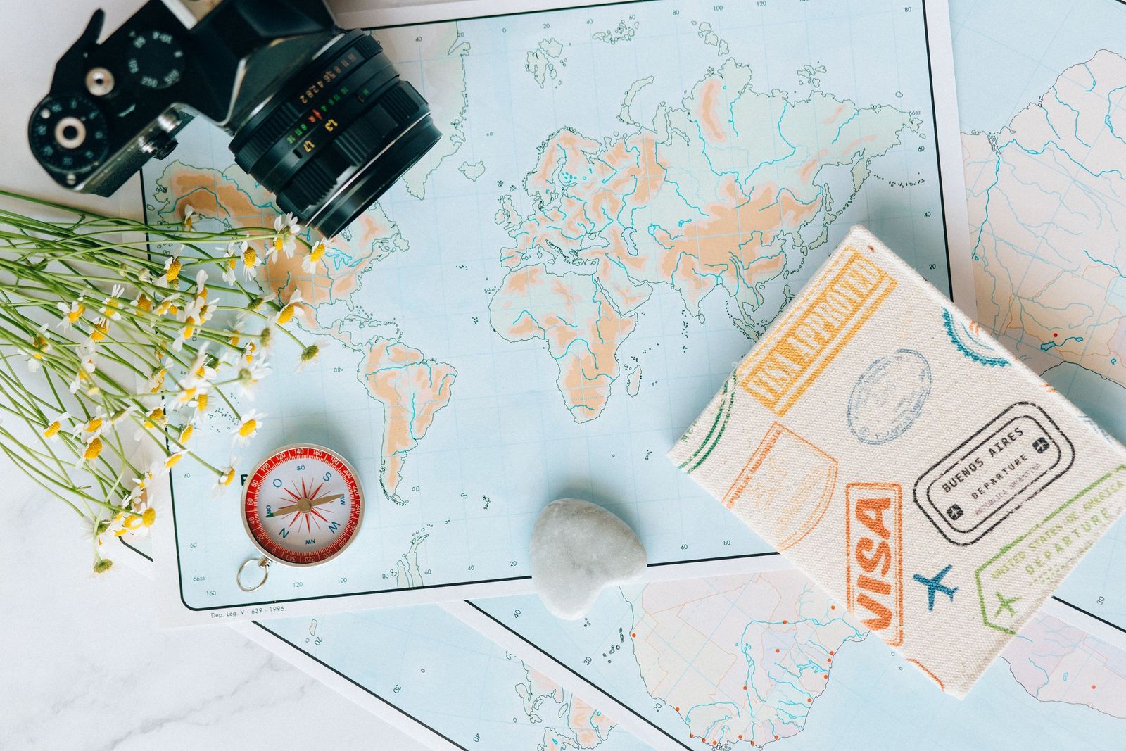 A world map with a compass, a camera and travel documents on a table