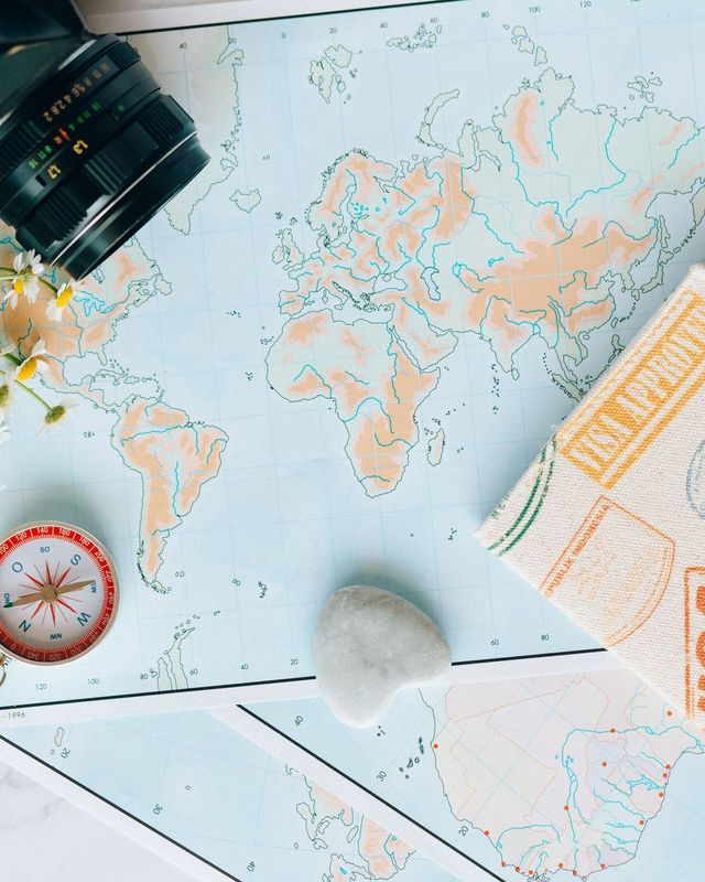 A world map with a compass, a camera and travel documents on a table